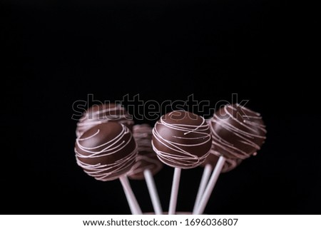 Cake pops in chocolate cream in the form of a bouquet stand in jars with sugar on a wooden background. Tasty food