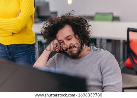 Closeup photo of a male employee with curly hair leaning on his hand on the office desk and sleeping