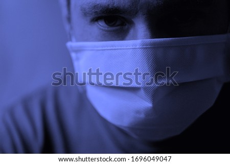 A man in a medical mask with a tired look looks directly at the camera. Quarantine and isolation. The worldwide tragedy and pandemic of the COVID-19 coronavirus. Royalty-Free Stock Photo #1696049047