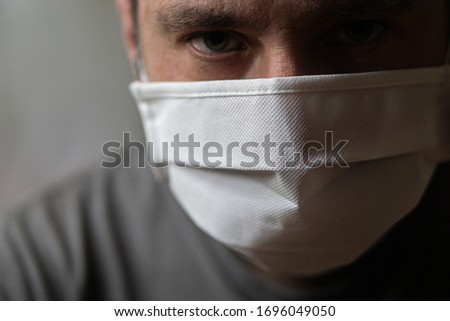 A man in a medical mask with a tired look looks directly at the camera. Quarantine and isolation. The worldwide tragedy and pandemic of the COVID-19 coronavirus. Royalty-Free Stock Photo #1696049050