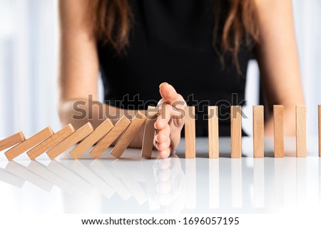 Woman hand stopping falling wooden dominoes effect on white solid ground Royalty-Free Stock Photo #1696057195
