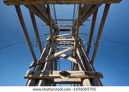 The support of a wooden bridge of logs and planks against a blue sky.