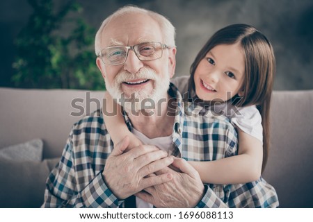 Closeup photo of funny two people old grandpa little granddaughter sitting sofa stay home quarantine safety hugging piggyback modern design interior living room indoors Royalty-Free Stock Photo #1696088113