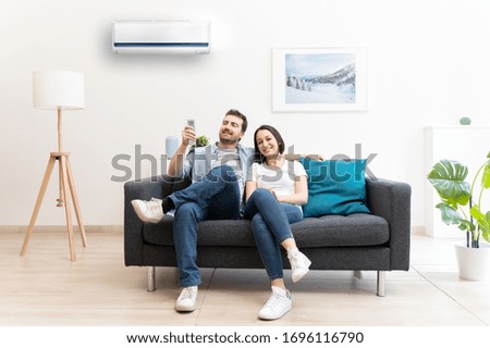 Happy couple freshen up using air conditioner at home Royalty-Free Stock Photo #1696116790