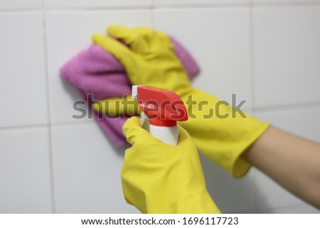 The washer is washing the white tile with yellow gloves.