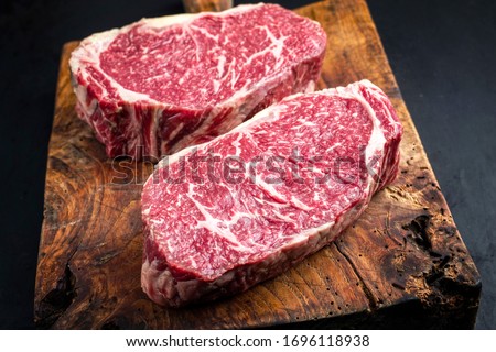 Raw dry aged wagyu entrecote beef steak roast as closeup on a rustic wooden cutting board  Royalty-Free Stock Photo #1696118938