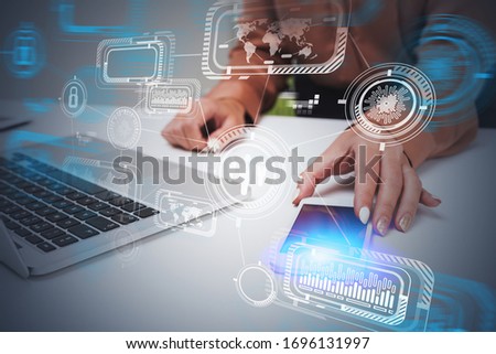 Hands of businesswoman using smartphone and laptop in blurry office with double exposure of futuristic HUD business interface. Concept of hi tech and infographics. Toned image