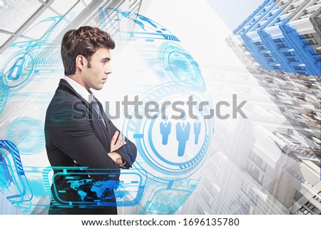 Portrait of confident young European businessman standing with crossed arms in abstract city with double exposure of blurry HUD infographic interface. Concept of hi tech and leadership. Toned image