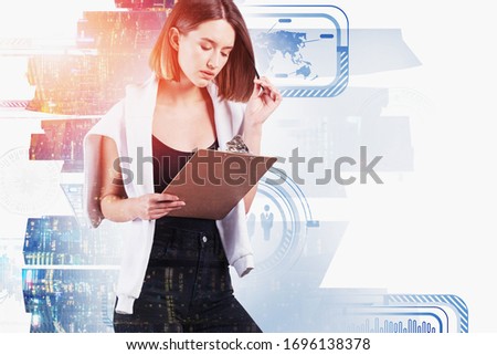 Thoughtful young European businesswoman reading financial report in abstract city with double exposure of blurry HUD business interface. Concept of hi tech. Toned image