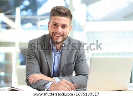 Portrait of happy businessman sitting at office desk, looking at camera, smiling. Royalty-Free Stock Photo #1696139317