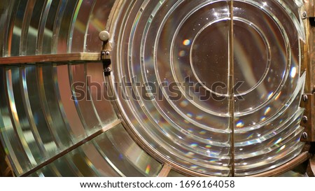 Fresnel lens with brass structure, nautical lighthouse tower. Detail of the glass lantern with rainbow spectrum. System of lamps and lenses to serve as a navigational aid. Old sea searchlight beacon