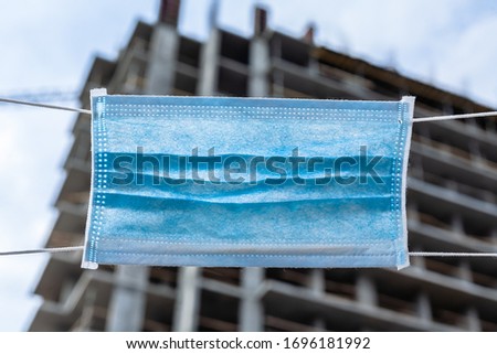 Construction in quarantine. Conceptual photo of a stop of construction work. Unfinished house is blocked by a medical mask.