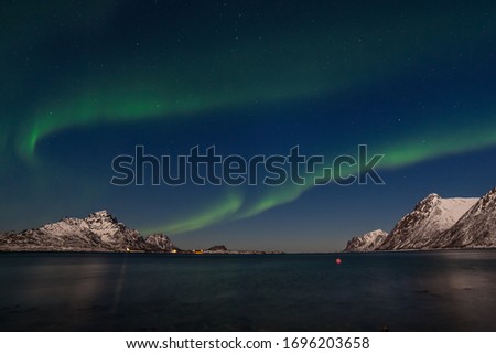Dramatic northern lights, Aurora borealis over fjord mountains with many stars on the sky in Lofoten islands, Norway, long shutter speed.