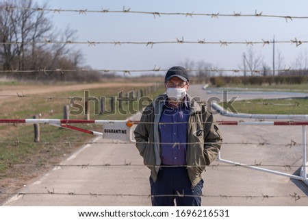 Man in medical mask behind barbed wire in quarantine zone.