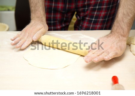 The white man's hands roll out the dough on a light table with a rolling pin. Cooking homemade cakes. Things to do at home.
