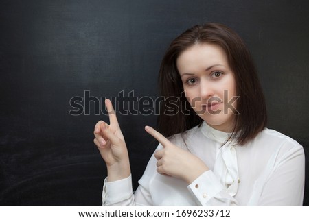 Young woman is smiling and pointing up, against black chalkboard