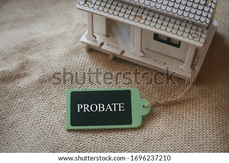 A toy wooden house on a rugs with a wooden tag written with word Probate. Royalty-Free Stock Photo #1696237210