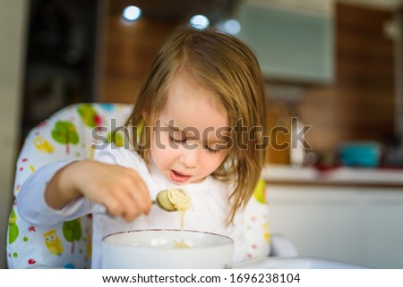Two years old eats chicken soup by herself with a spoon. Child development concept