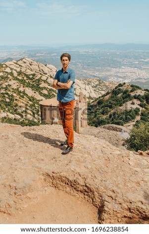 A male traveller enjoys views from the mountains of Montserrat in Spain. A man in beige trousers and a blue t-shirt against the backdrop of Montserrat