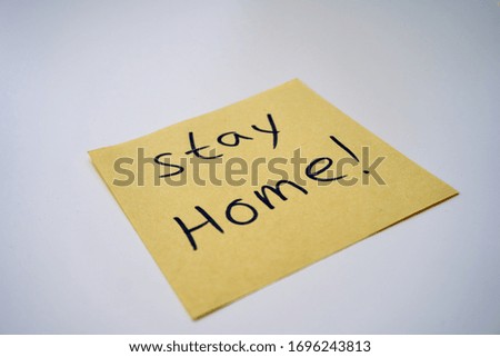 Yellow sticky note with "Stay Home" written with pen on white background, self isolation and home quarantine from Covid-19 coronavirus
