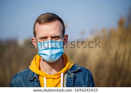 Close up portrait of a man outdoor in a surgical mask with rubber ear straps. Typical three-layer surgical mask for covering the mouth and nose. Bacteria mask procedure. Protection concept.