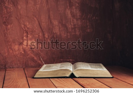 Open bible on a red old wooden table. Beautiful brown wall background.	
