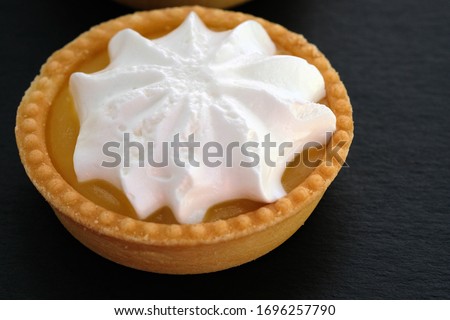 Tartlet with lemon cream and whipped squirrels. Round cake on a shortcrust pastry. Shortcrust tartlet and whipped cream on a black background.