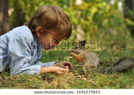 the cute kid boy feeding the squirrel in sunny forest