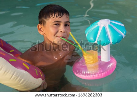 boy with a rubber ring and with a refreshing drink, swims in the pool, the concept of rest and vacation