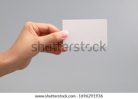 Hand holding an empty white business card on grey background
