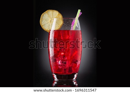 glass with red drink with ice, straws and lemon on black background