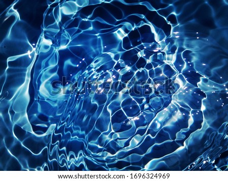 The​ abstract​ of​ surface​ blue​ water​ use​ for​ graphic​ design.  The​ pattern​ of​ surface​ blue​ water​ in​ swimming​ pool​  reflected​ with sunlight​ for background. Water​ splashed​ 