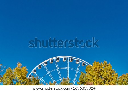 A closeup shot of a Ferris wheel near trees under a blue clear sky