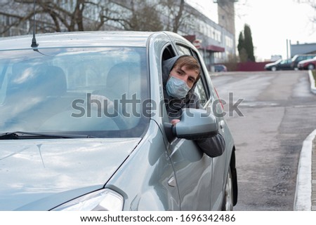 A man driving a car rides in a city, having escaped his head from the window. A one-time medical mask is on the face. Elimination for Coronavirus, viruses and bacteria transmitted by the air output.  Royalty-Free Stock Photo #1696342486