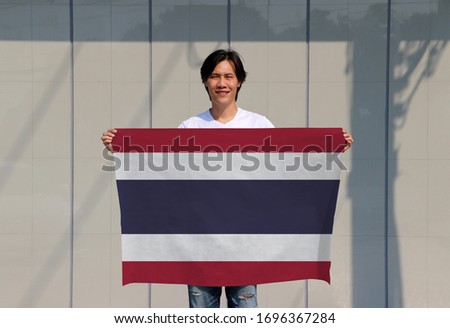 The man is holding Thailand flag in his hands on grey background.