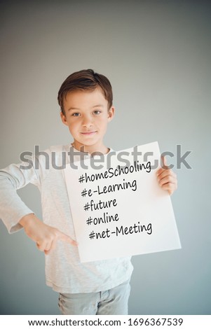 boy holding white sign with the words homeschooling and more in front of grey background during corona crisis