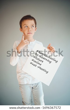 boy holding white sign with the words homeschooling and more in front of grey background during corona crisis
