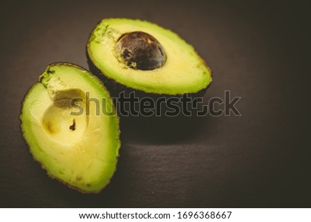 Close-up of an avocado and avocado on black background. Healthy food concept. Fresh, raw avocado on a black background. Green ripe avocado from organic avocados plantation - healthy food