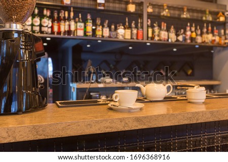 Bar counter with cup and white teapot, blurred alcohol bottles assortment on background. Barroom in restaurant, hotel, pub, cafe, copy space. Royalty-Free Stock Photo #1696368916