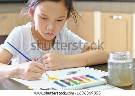 Cute Asian child girl is holding paintbrush and painting on the paper. Selective focus