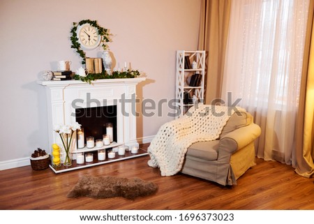 Classic white interior of living room with sofa near fireplace. Fireplace decorated with flowers and books. Cozy home interior