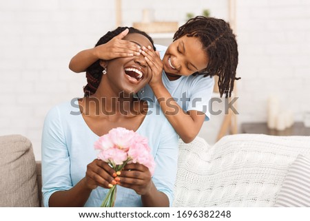 Surprise Concept. Laughing african woman holding flowers, little girl covering her eyes, copyspace Royalty-Free Stock Photo #1696382248