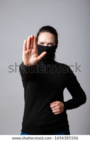 Girl in a black turtleneck pulled over her face showing a stop sign
