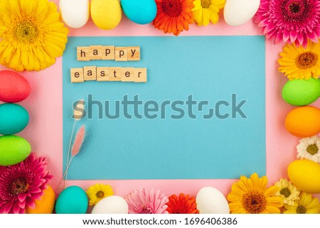 The inscription "Happy Easter" made of wooden cubes and beautiful spring composition of colored eggs and fresh flowers on a pink and blue pastel background. Template for design. Copy space.