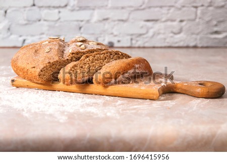 fresh home baked healthy bread from rye flour with pumpkin seeds on wooden rustic cutting board on marble countertop in bright kitchen