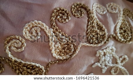 Embroidered pattern tablecloth closeup. Ornate textile texture with traditional ornaments in shades of beige and light brown on crumpled satin surface. Retro embroidery backdrop.