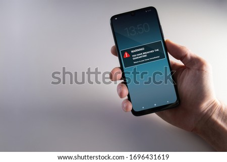 Quarantine breach warning notification mockup on smartphone held in hand. Advice to stay in home quarantine to stop contagion. Pandemic, healthcare, technology and privacy Royalty-Free Stock Photo #1696431619