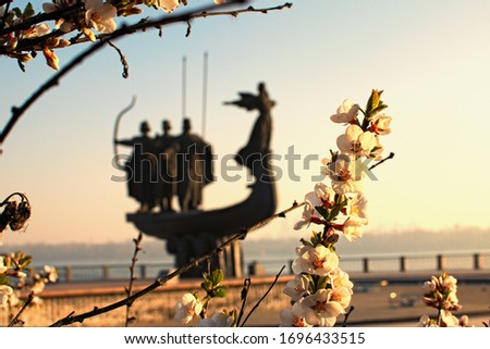 White blossom flowers on tree branch in sunny spring morning. Blurred silhouette of Monument to legendary founders of Kyiv: Kiy, Schek, Khoryv and their sister Lybid in the background. Kyiv, Ukraine.