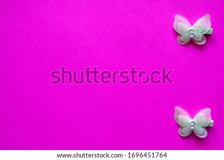 two beautiful, children's hair clips, in the shape of a butterfly, yellow with beads, lies vertically against a bright raspberry background. Place for text, beauty and style from childhood.