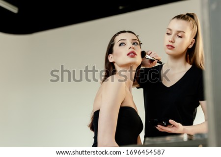 selective focus of young makeup artist applying face powder on beautiful model